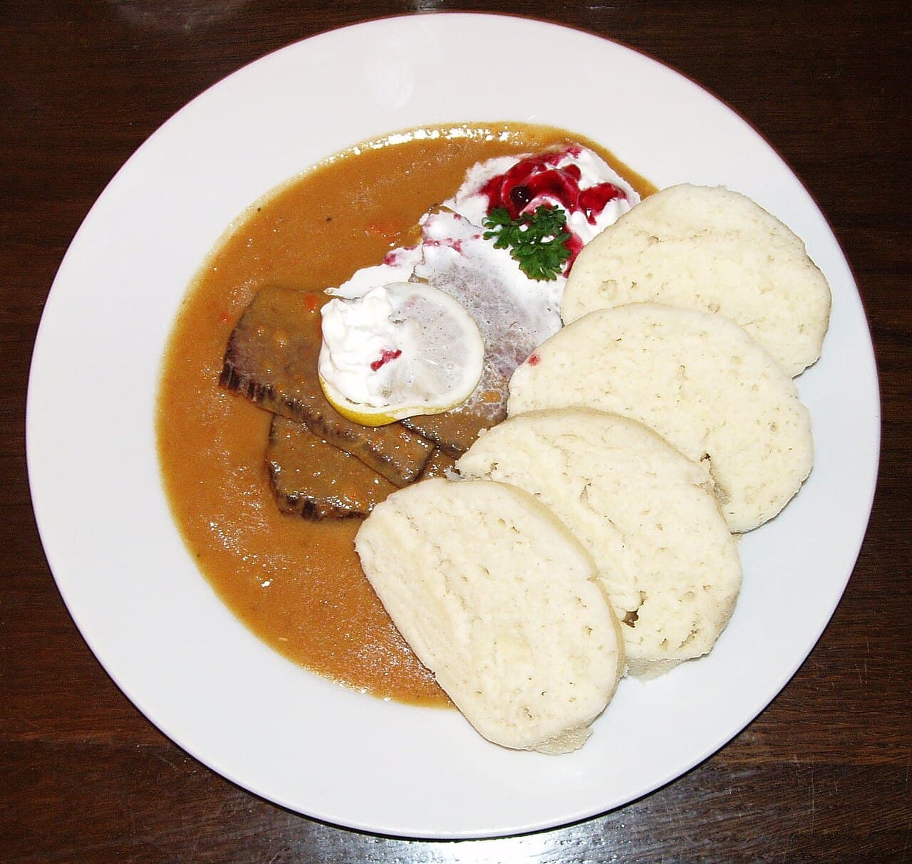 A plate of svíčková - sliced beef in cream sauce with bread dumplings, cranberries and whipped cream