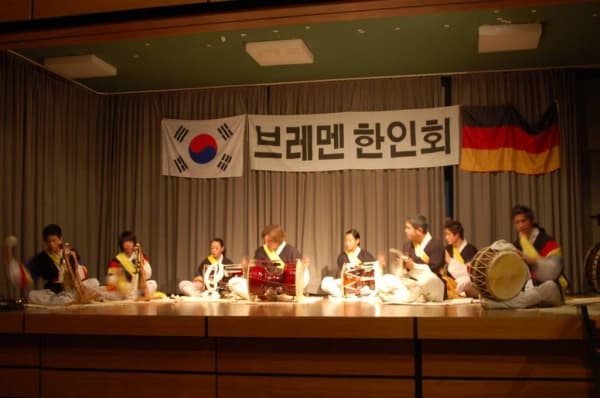 Four musicians in colourful Korean costumes playing large drums and gongs