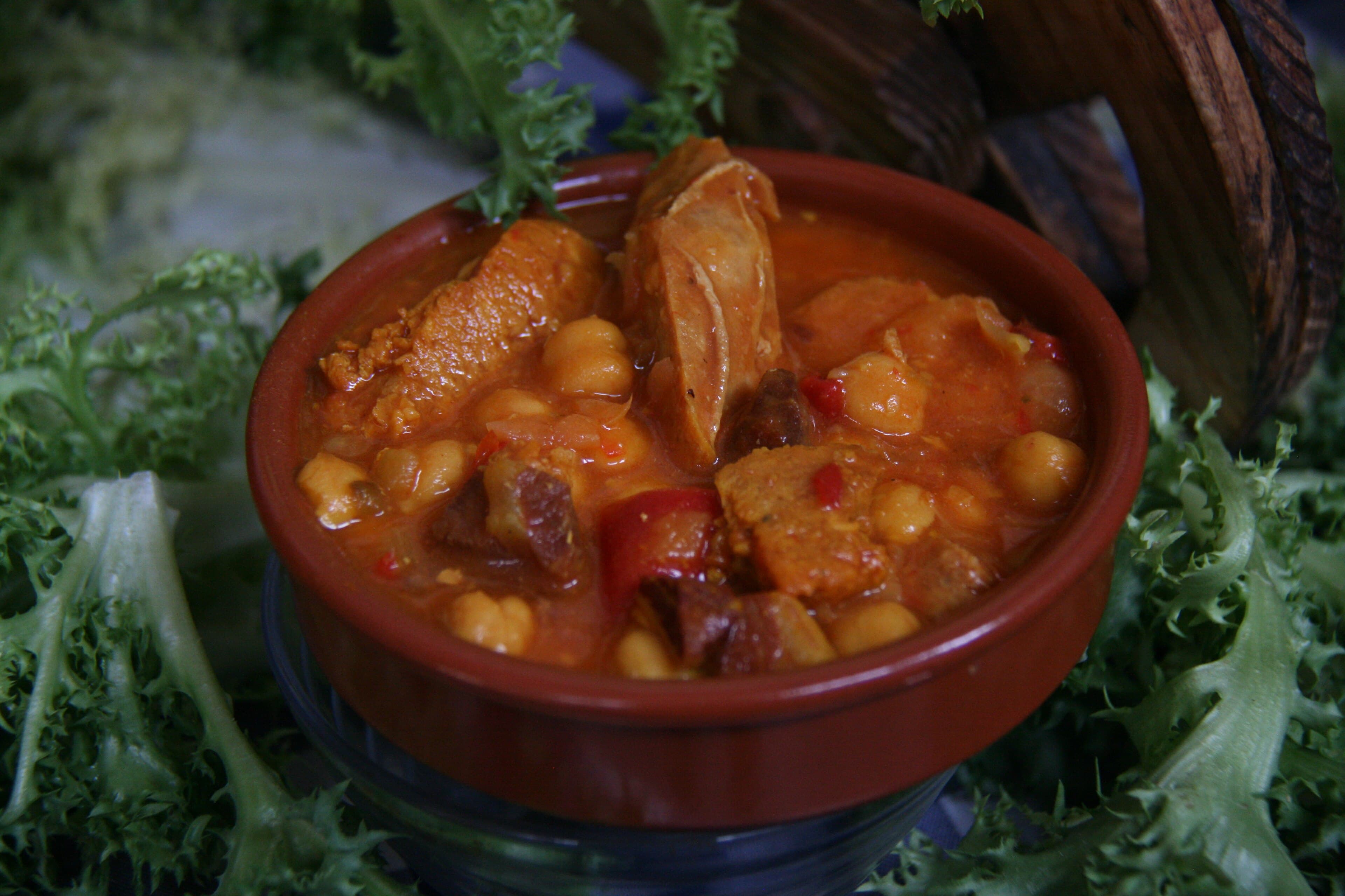 A steaming bowl of escudella stew with pasta and vegetables on a wooden table