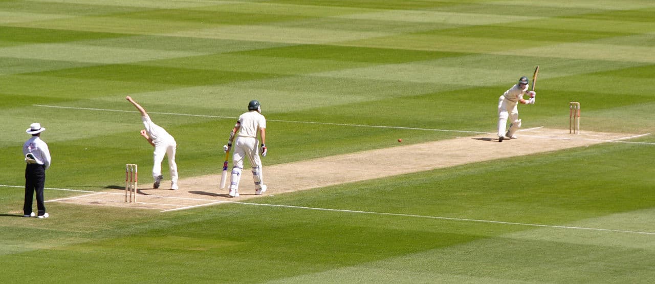 A cricket match being played on a lush green ground in Barbados under a blue sky