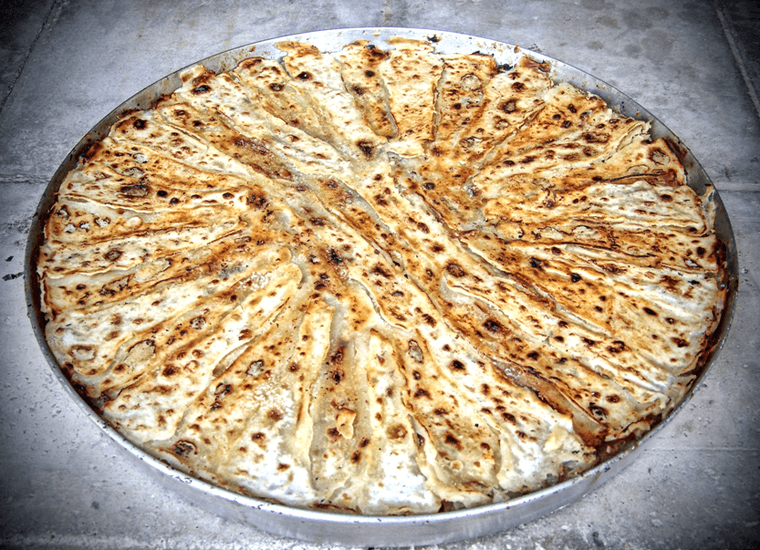 A round flia layered pancake being cooked over an open fire with cream between the layers