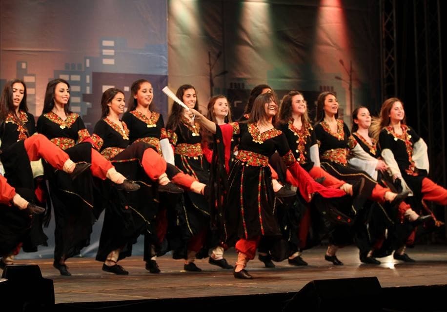 A line of dancers performing dabke, holding hands and kicking in unison