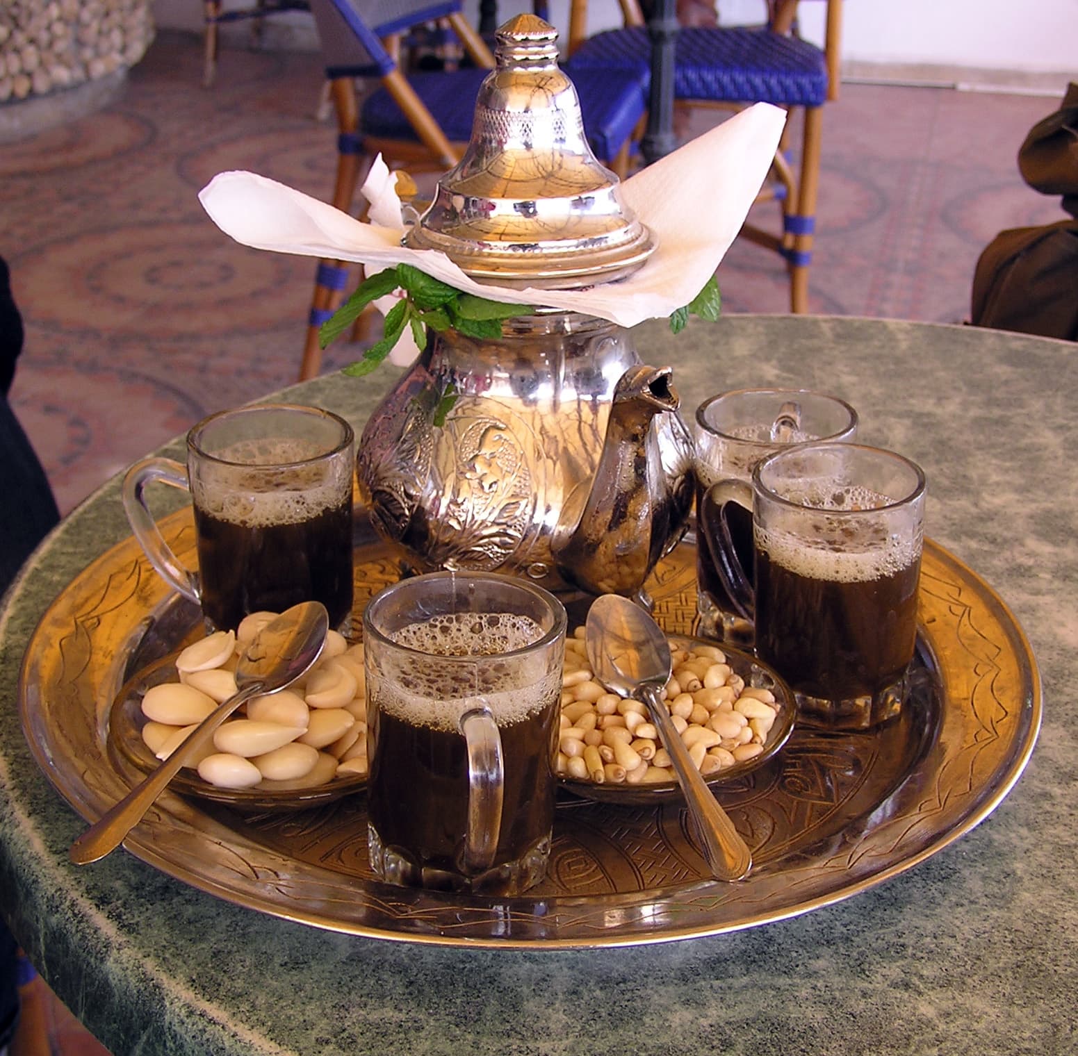 A glass of bright green mint tea being poured from a teapot with a stream of froth on top