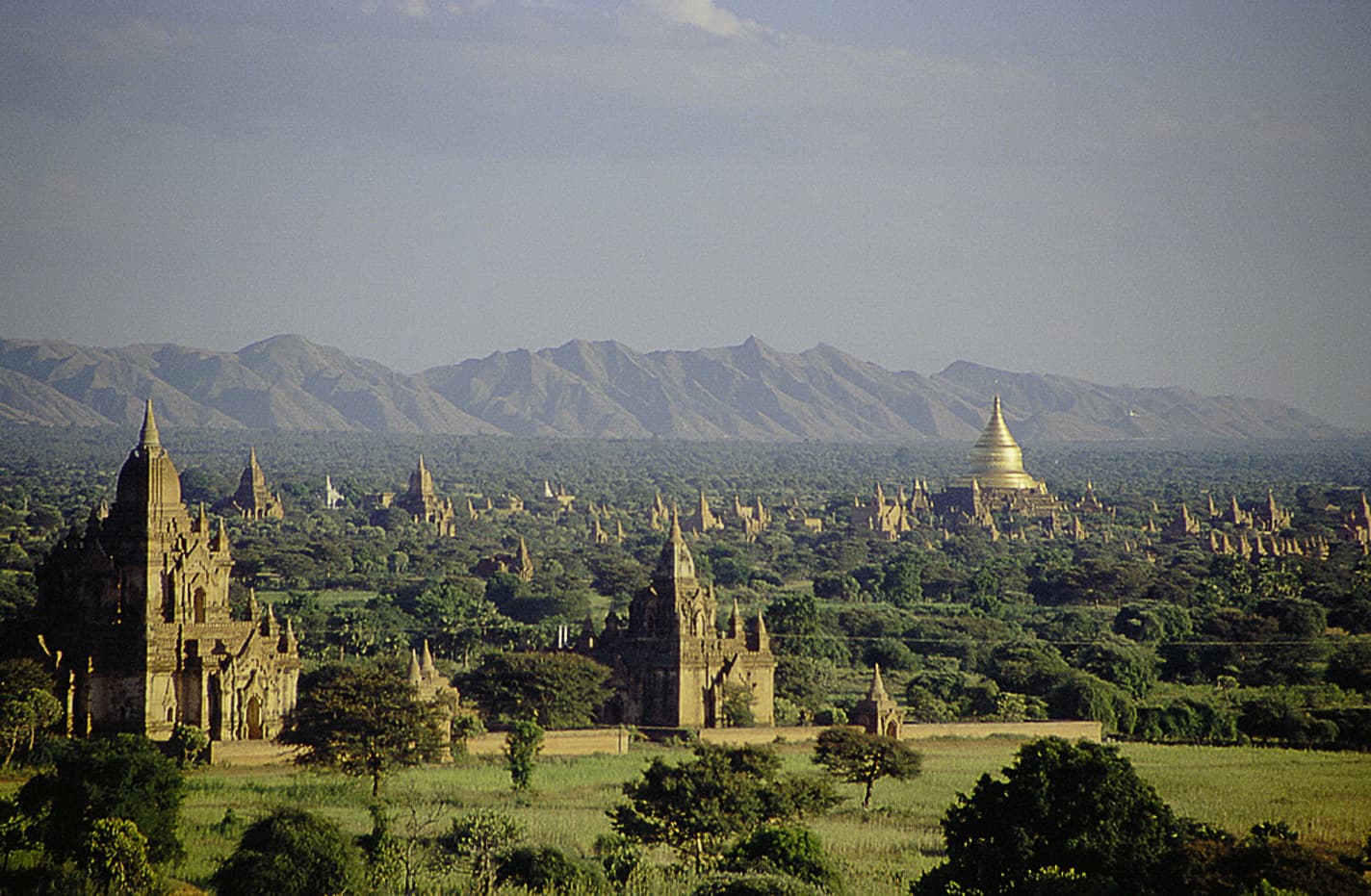 Brick temples rising out of green trees across the plain of Bagan at sunrise