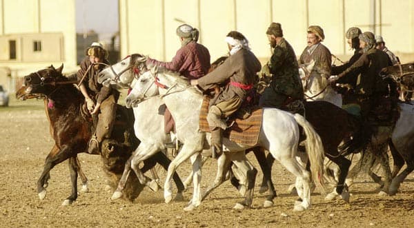 Riders on galloping horses in colourful traditional dress competing in a buzkashi game