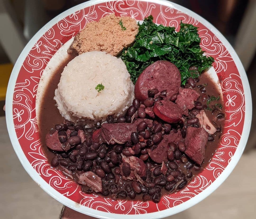 A pot of dark bean stew with herbs being ladled into a bowl